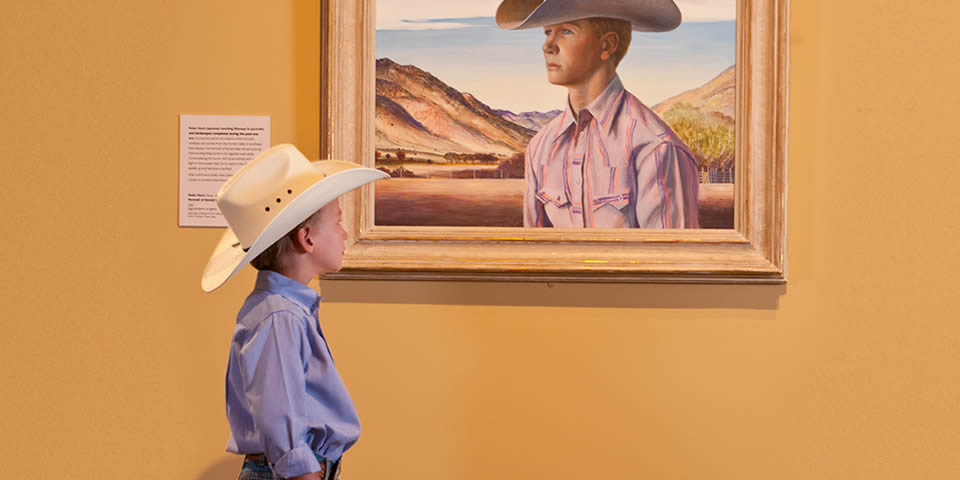 programs-cowboy young man wearing a cowboy hat looking at a painting of a young man wearing a cowboy hat.