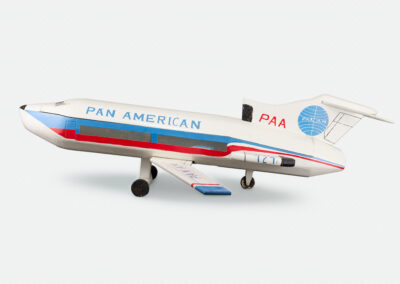 Wooden coffin carved and painted as a Pan American 727 jetliner, white with blue and red stripes, the Pan Am globe logo on the tail, and landing gear, shown in profile against a light gray background.